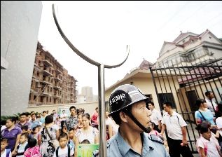 學校門口，保安頭戴鋼帽手拿鋼叉站在校門口，護衛學校安全。